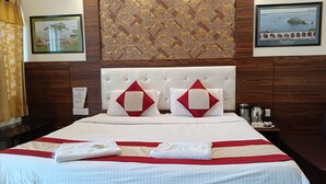 A hotel room with a large bed, two pillows, a headboard, a nightstand with a coffee maker, and framed pictures on the wall. - Hotel Sidhartha (Agra)