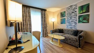 A hotel room with a desk, chair, sofa, and a large window with curtains.