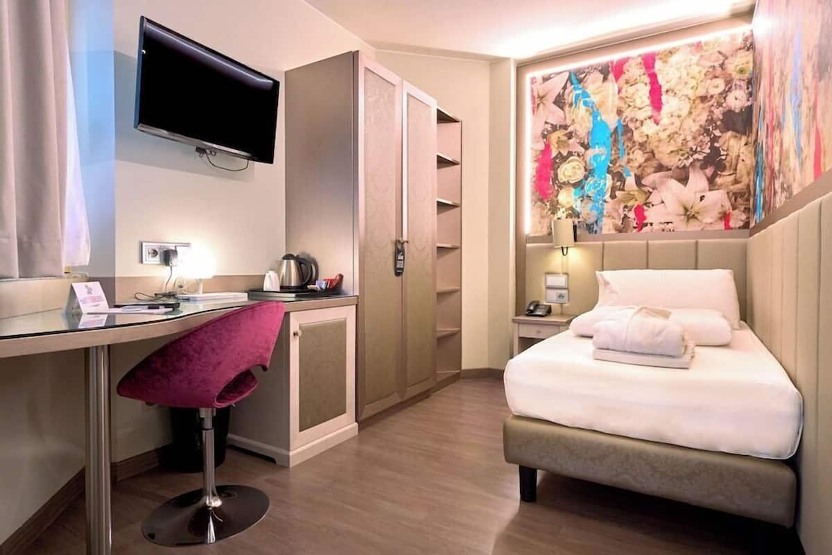 Una habitación de hotel con cama, escritorio, silla, televisión y un mural floral en la pared.