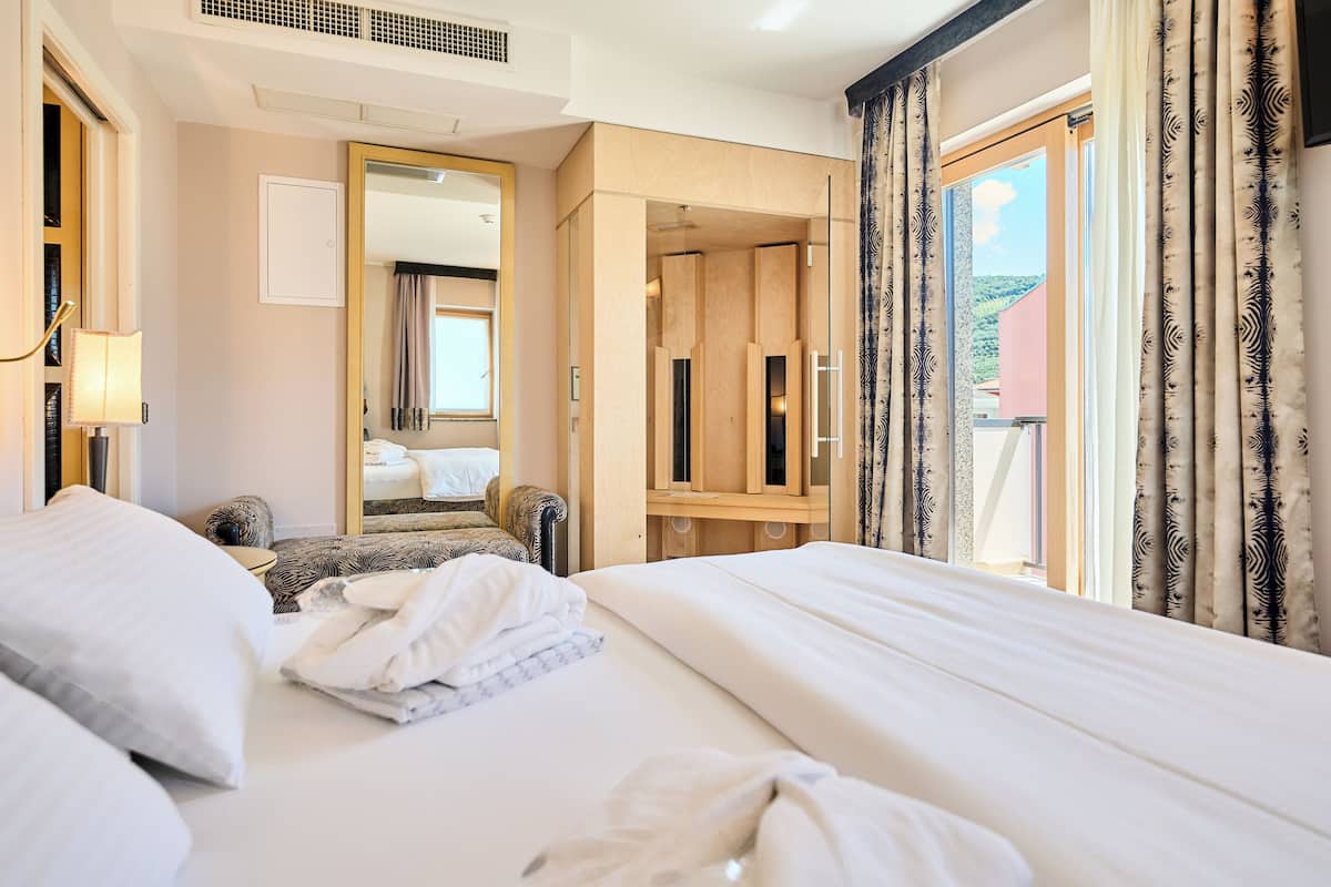 Habitación de hotel con una cama grande, una zona de estar con una silla, un armario de madera y un espejo amplio.