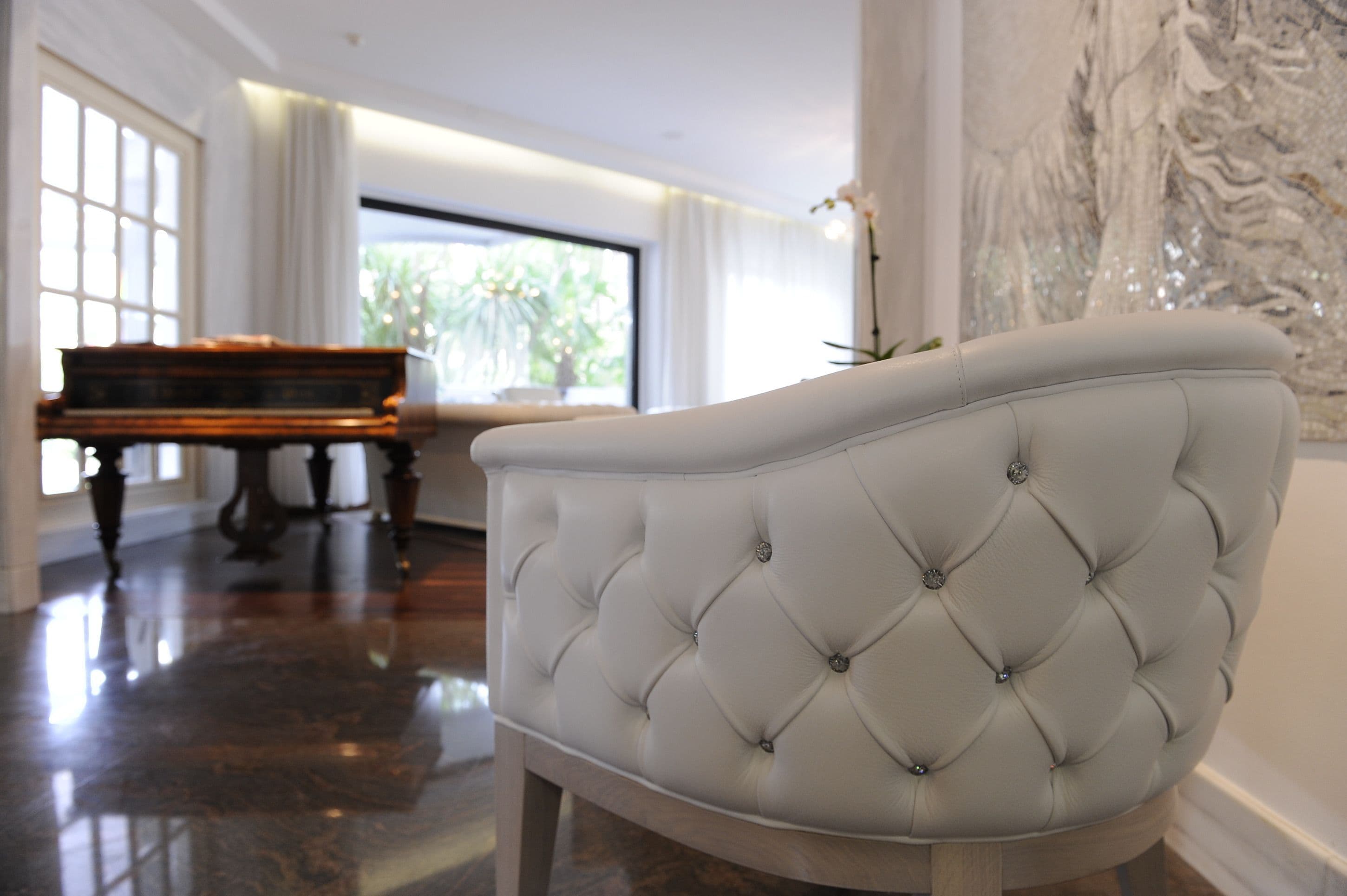 Una silla blanca con capitoné en una habitación bien iluminada, con un piano al fondo.