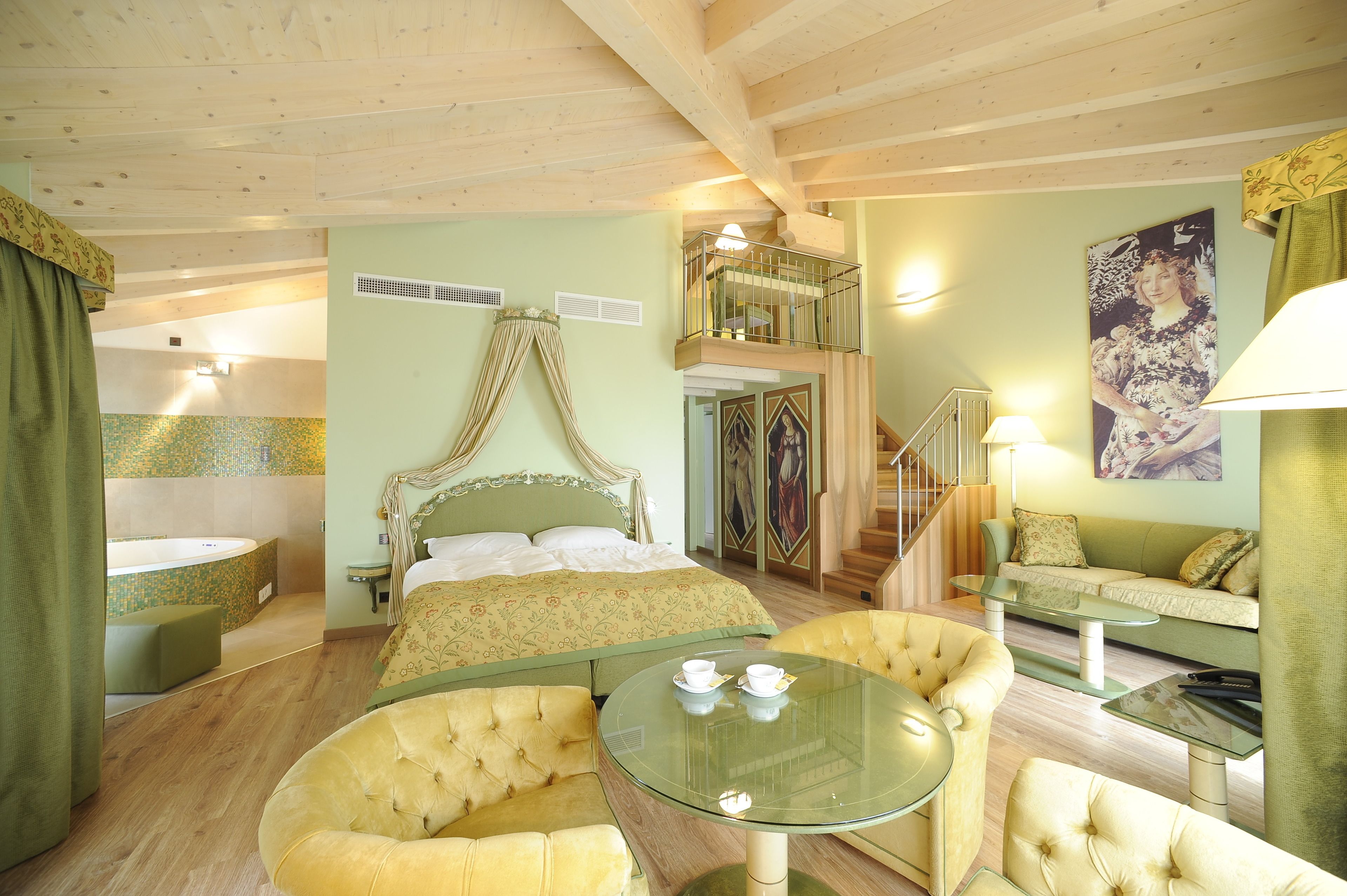 Habitación de hotel con una cama, una mesa de vidrio, dos sillones, un sofá, un balcón y una escalera.