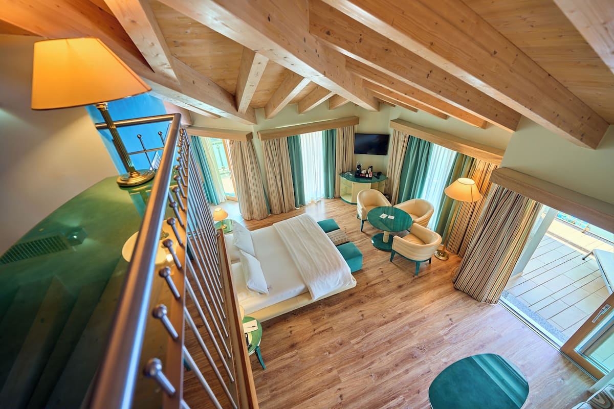 Habitación de hotel con techo de madera, cama con ropa blanca, sofá verde, una mesa redonda y un televisor.