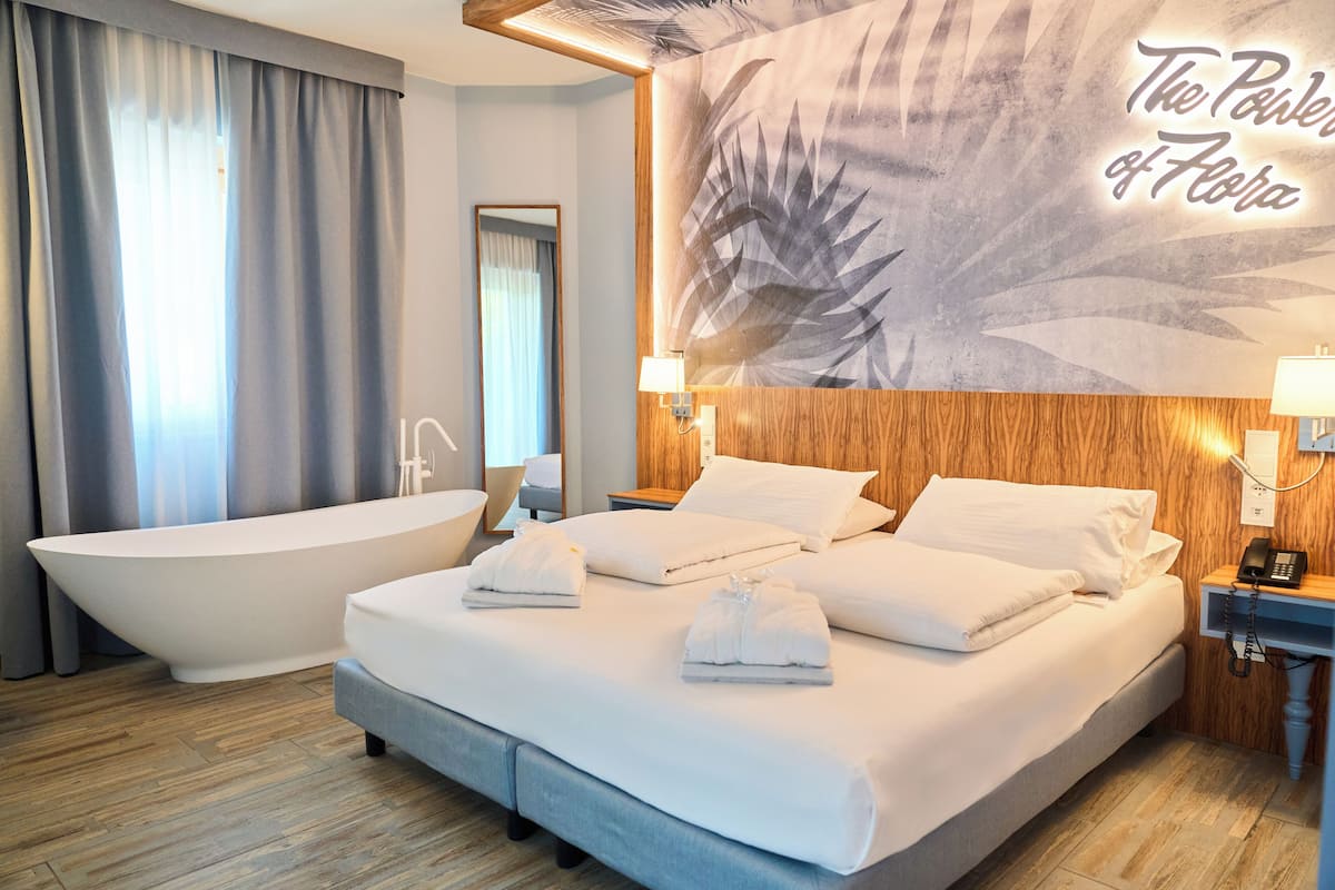 Una habitación de hotel con una cama grande, una bañera, un panel de madera y un mural en la pared.