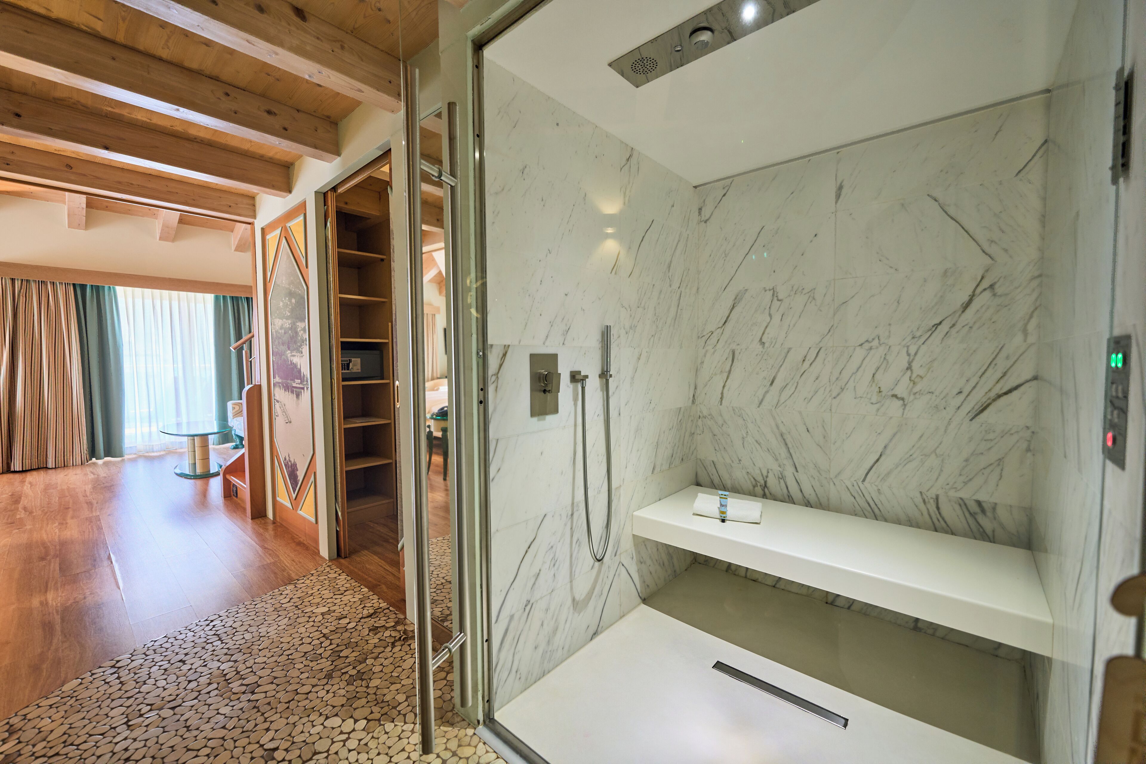 A modern bathroom with a glass-enclosed shower, marble walls, and a wooden floor.