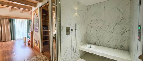 Een moderne badkamer met een douchecabine van glas, marmeren wanden en een houten vloer.