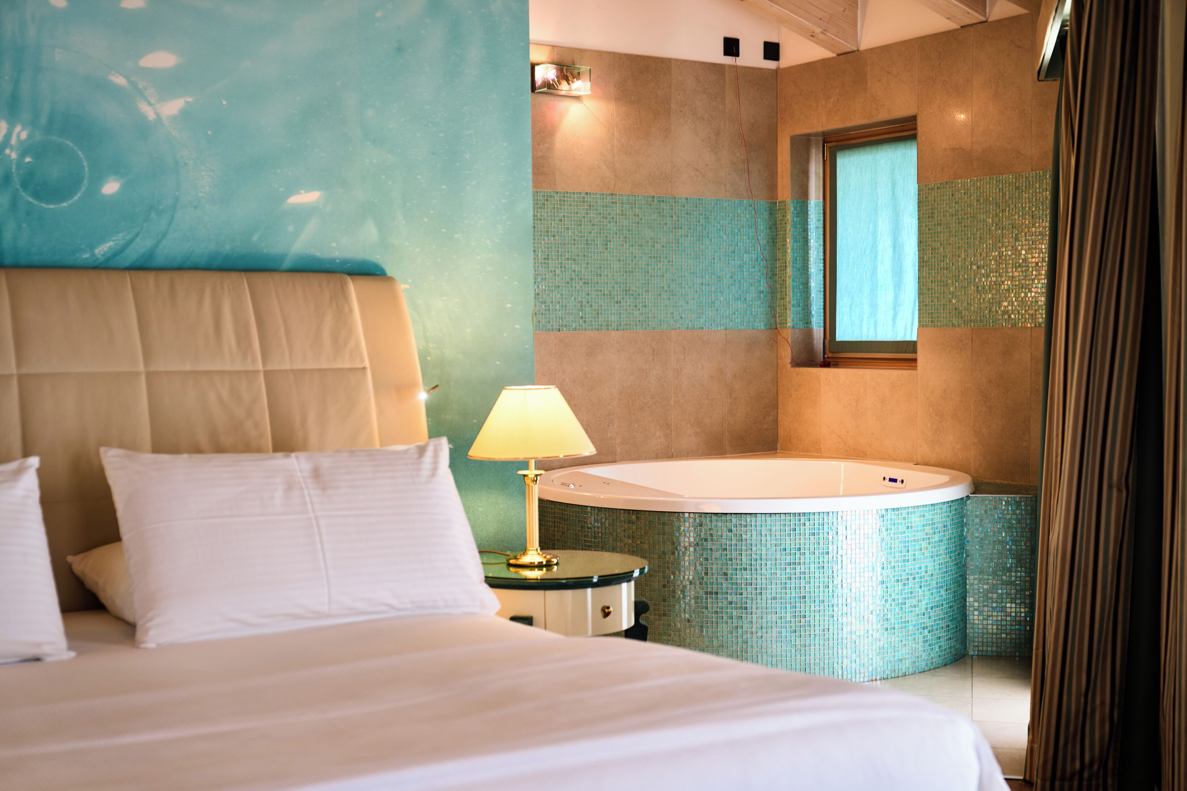 A hotel room with a bed, a nightstand, a lamp, and a bathtub.