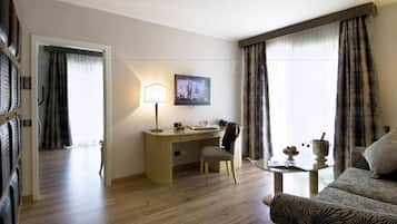 A hotel room with a wooden desk, a chair, a television, a sofa, and a small table with a lamp and decorative items.