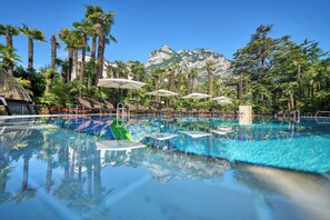 A pool with clear water, surrounded by palm trees and a mountain backdrop. - Parc Hotel Flora (Riva del Garda)