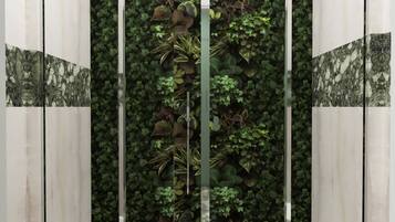 Un baño con separador de vidrio, dos lavamanos blancos y una pared cubierta de plantas verdes.