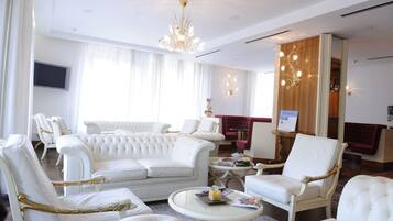 A spacious living room with white upholstered furniture, a chandelier, and a television mounted on the wall.
