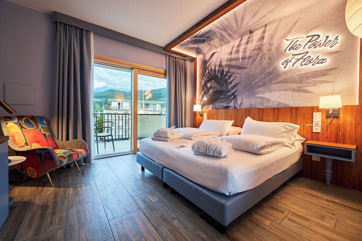 Habitación de hotel con una cama grande, una silla colorida, vistas a las montañas y un diseño floral en la pared.