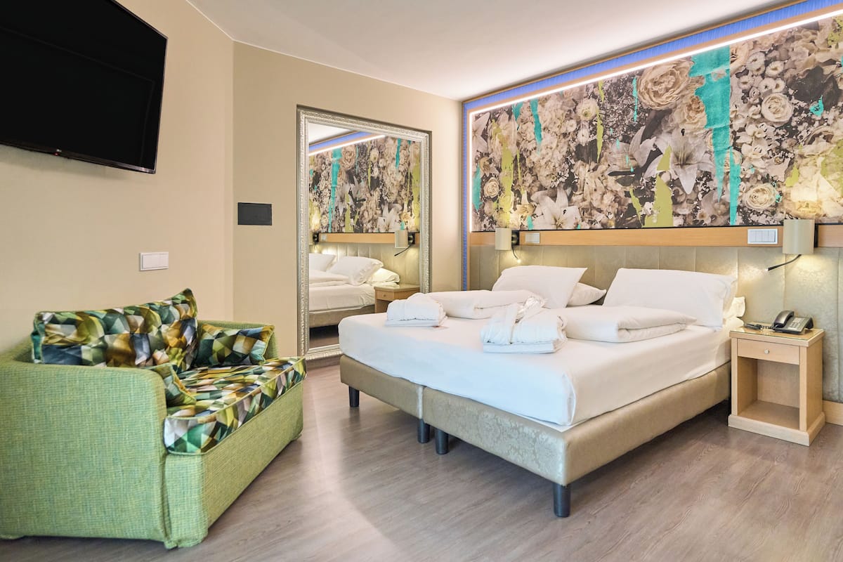 Una habitación de hotel con una cama grande, un sofá verde, un televisor de pantalla plana y un mural floral en la pared.