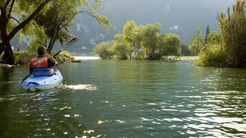A person kayaking on a river surrounded by trees and a distant castle-like structure.