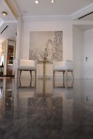 Un vestíbulo moderno con dos sillones blancos, una mesa redonda y un cuadro abstracto grande en la pared.