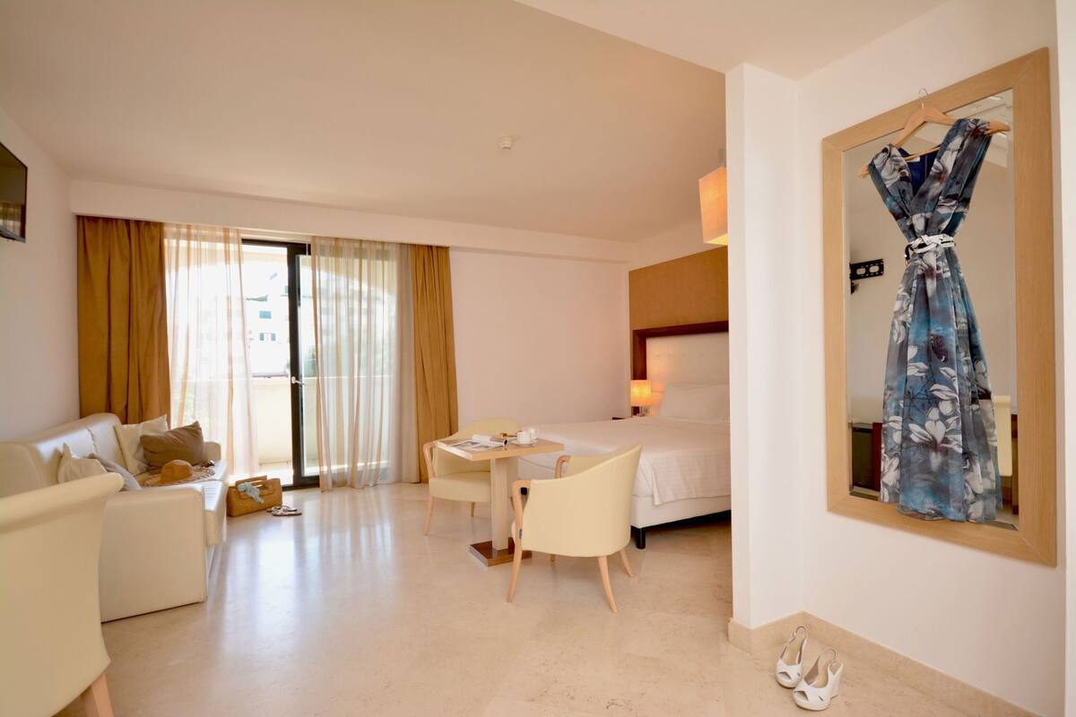 Une chambre d’hôtel comprenant un lit, un bureau, une chaise, un canapé et un grand miroir.