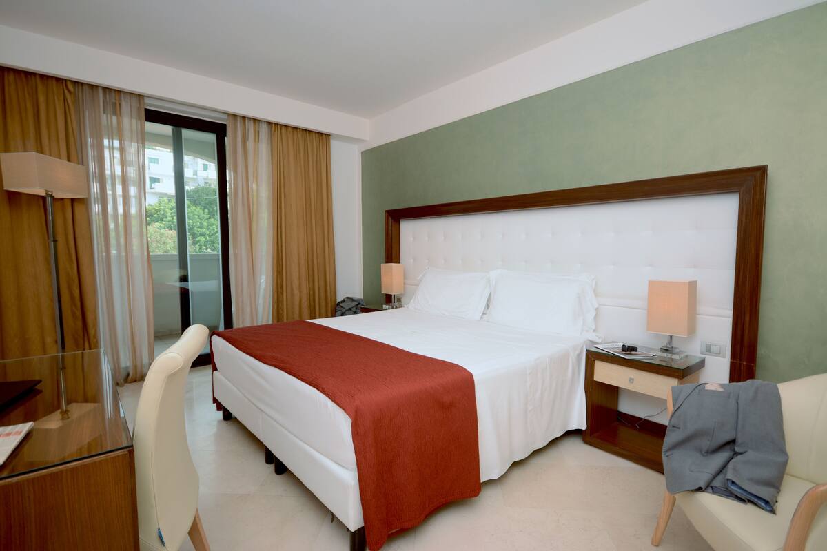 Une chambre d’hôtel avec un grand lit, un bureau, une chaise, une table de chevet et une vue sur la verdure.