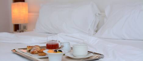 Ein Tablett mit Frühstücksangeboten auf einem Bett, darunter Gebäck, eine Tasse Tee und ein Glas Saft.