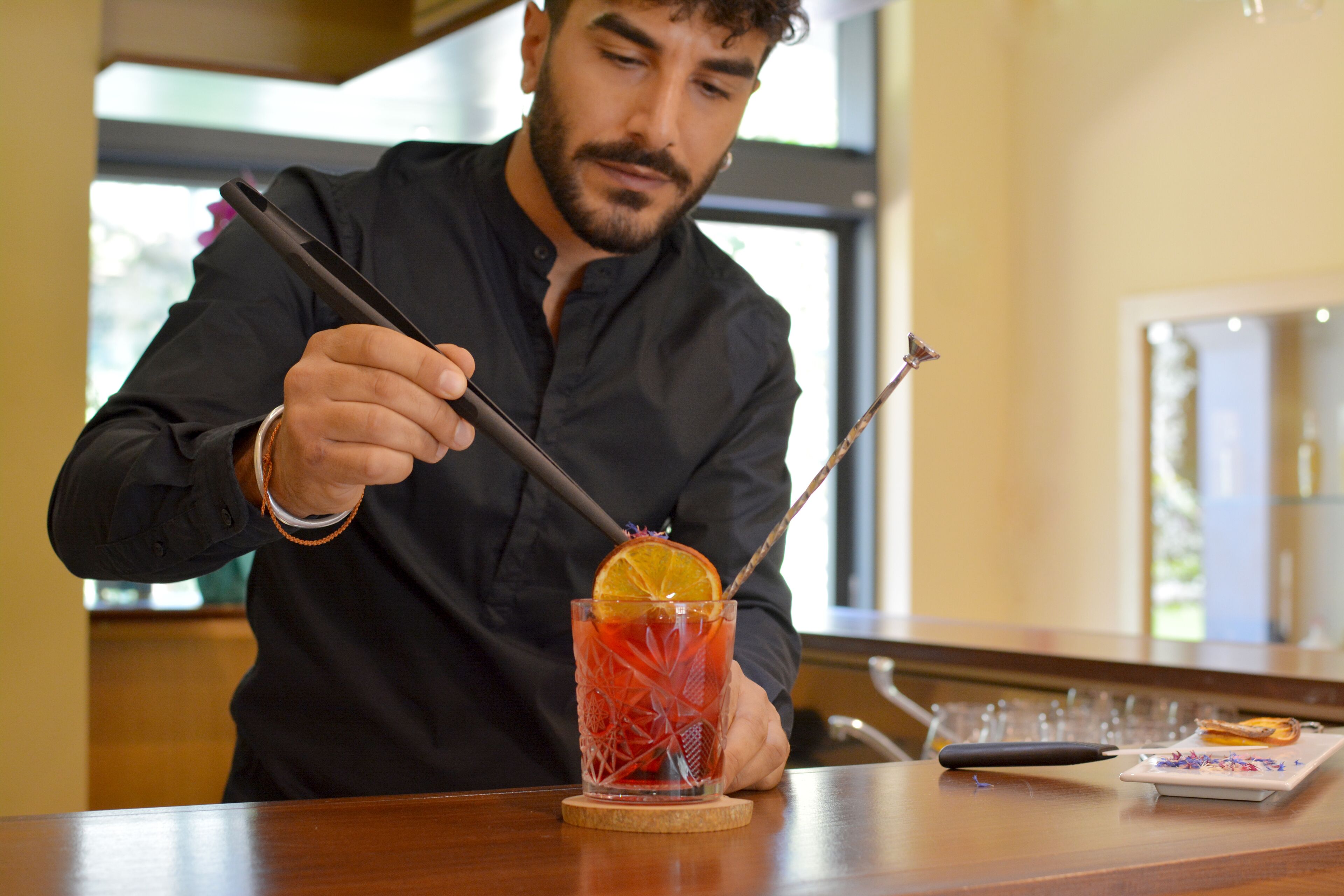Una persona preparando una bebida en un bar, con un vaso, una pajita y un coctelero.