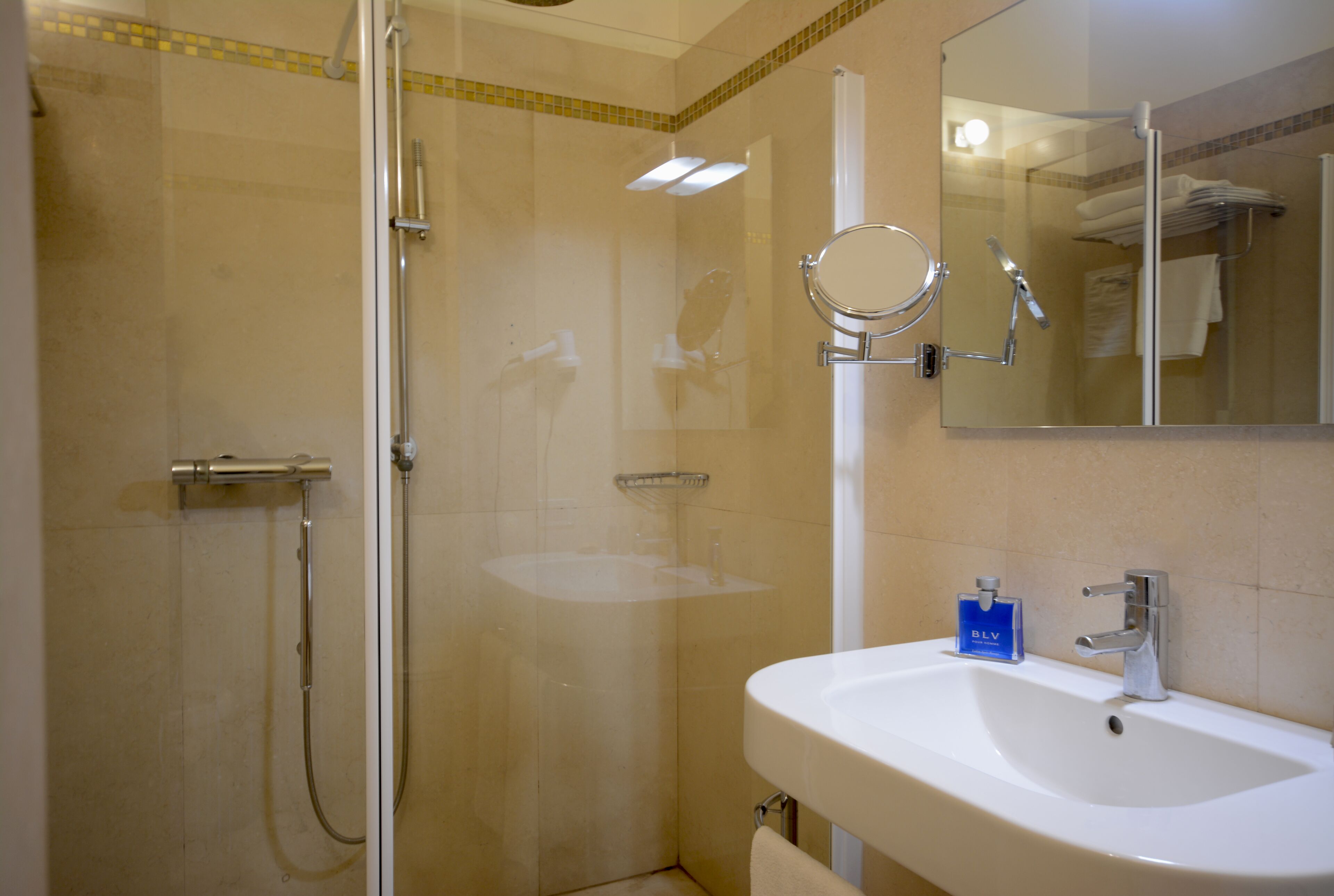 Bagno con doccia vetrata, lavandino con specchio e una boccetta di sapone BLV blu.