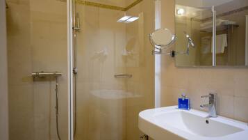 Un baño con ducha envuelta en vidrio, un lavamanos con espejo y una botella azul de jabón BLV.