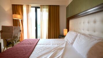 Ein Hotelzimmer mit einem großen Bett, einem Sessel, einem Schreibtisch und einem Fenster mit Vorhängen.