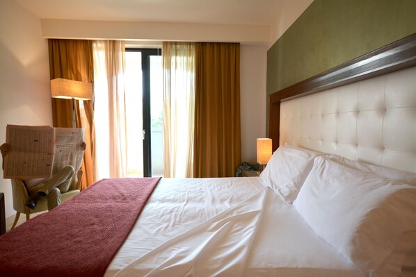 Une chambre d’hôtel avec un grand lit, une chaise, un bureau et une fenêtre avec des rideaux.
