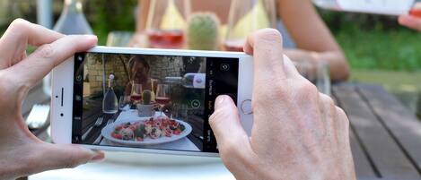 Una persona sosteniendo un teléfono inteligente, grabando una escena con una mesa dispuesta para una comida, una botella de vino y una copa.