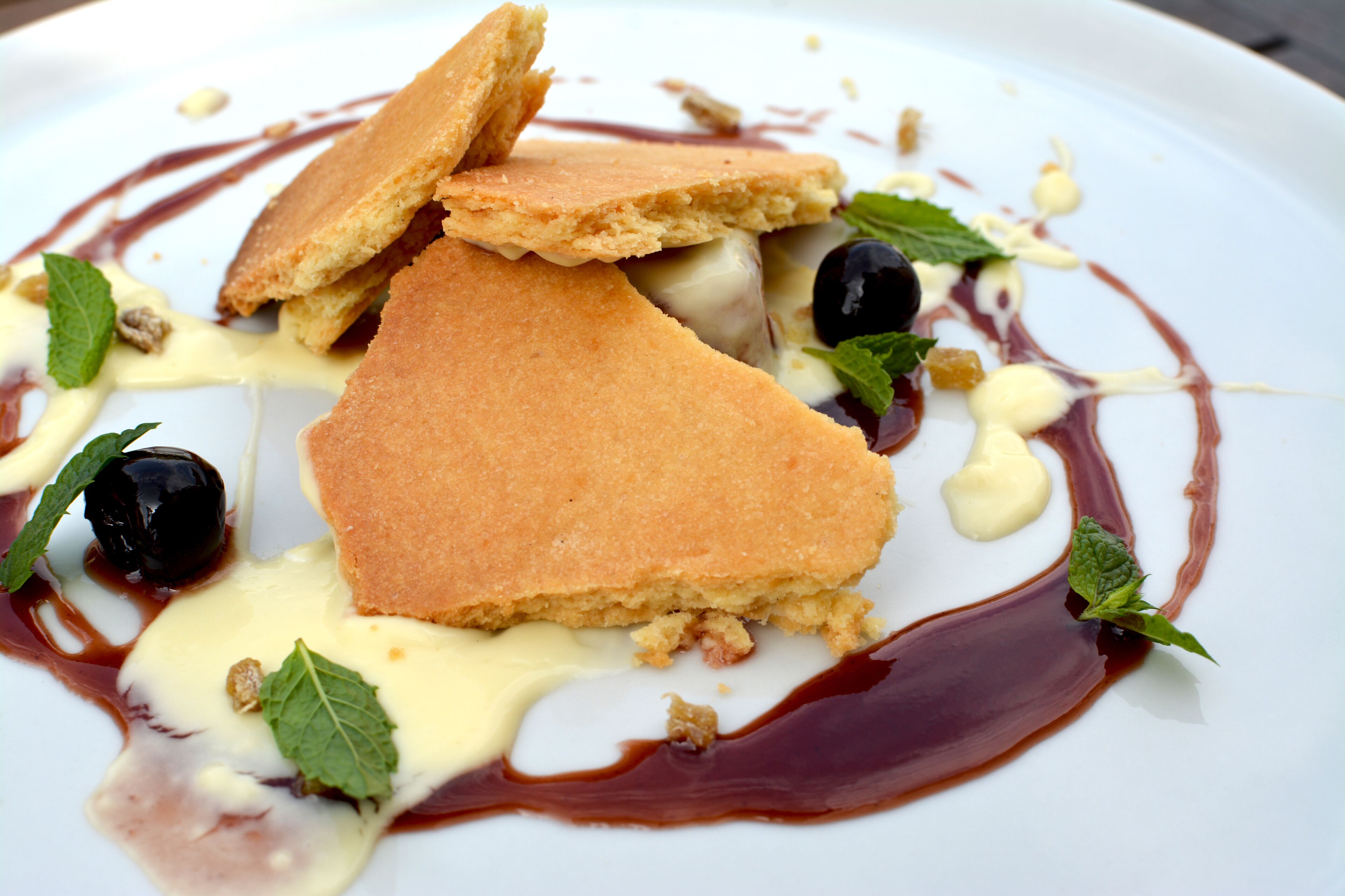 A dessert plate with triangular pastries, black olives, and mint leaves.