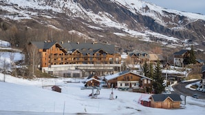 A mountain lodge with multiple wooden buildings, ski lifts, and a snowy landscape with mountains in the background. - Noemys les Terrasses de la Toussuire  (Saint-Pancrace)