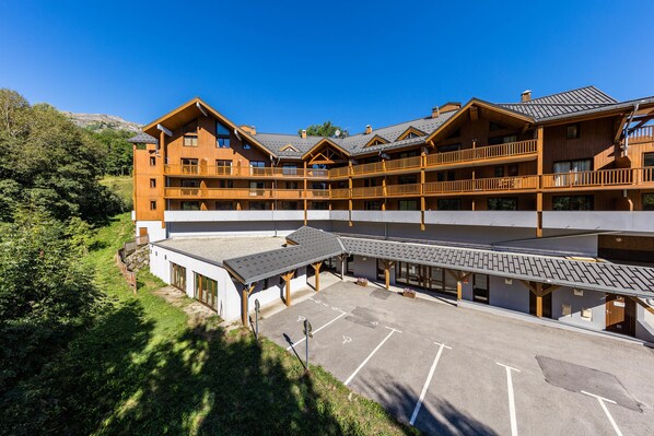 A multi-story wooden building with balconies, a covered parking area, and a mountainous backdrop. - Noemys les Terrasses de la Toussuire  (Saint-Pancrace)