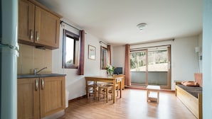 A modern kitchen with wooden cabinets, a dining table with chairs, a small bench, and a large sliding glass door leading to a balcony. - Noemys les Terrasses de la Toussuire  (Saint-Pancrace)