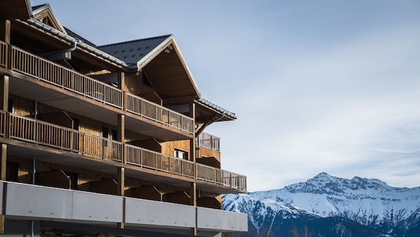 A multi-story building with balconies, wooden exterior, and a view of snow-capped mountains. - Noemys les Terrasses de la Toussuire  (Saint-Pancrace)