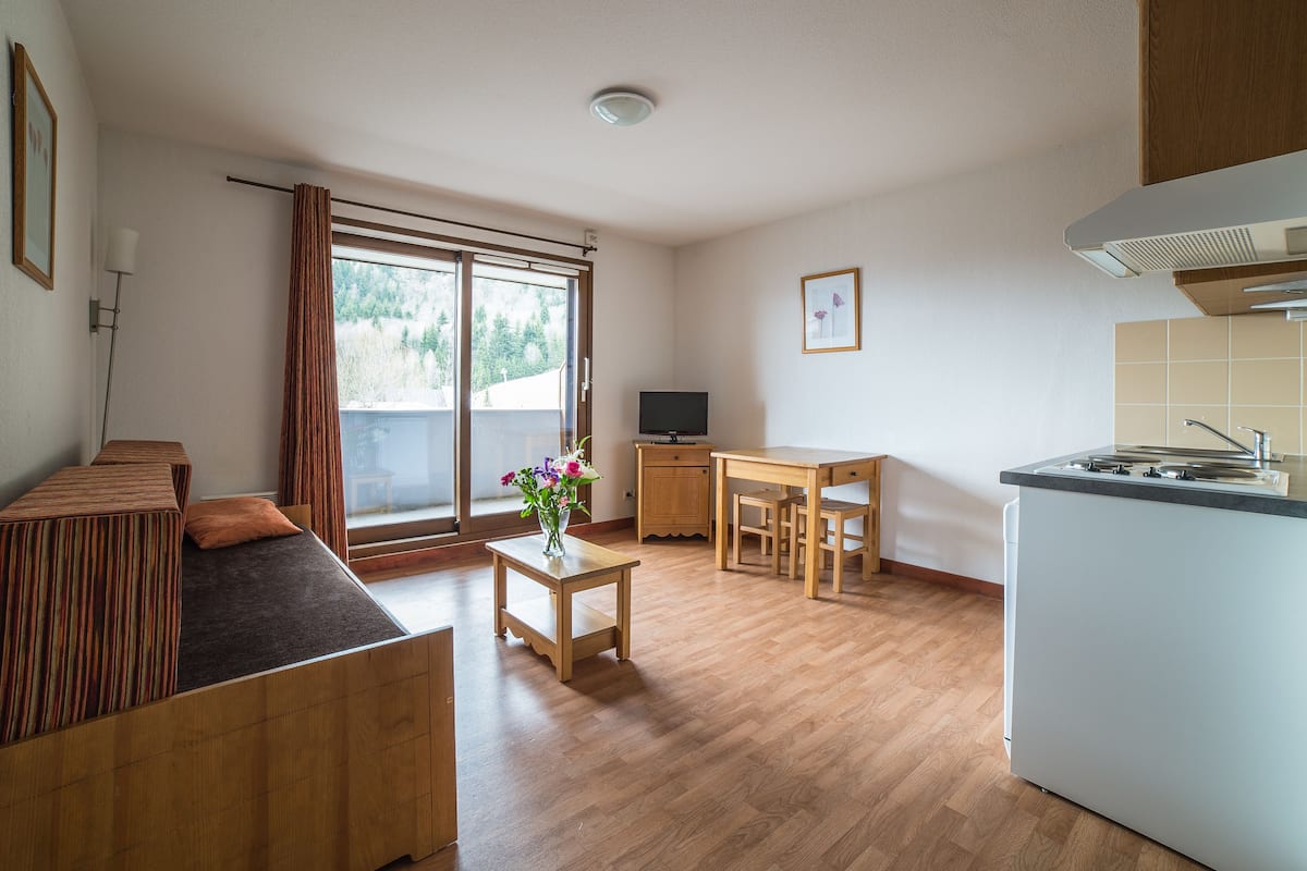 A modern apartment with a wooden floor, a dining area, a kitchen with a stove, and a large window with curtains.