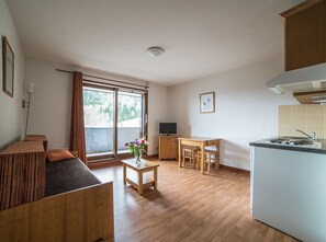 A modern apartment with a wooden floor, a dining area, a kitchen with a stove, and a large window with curtains. - Noemys les Terrasses de la Toussuire  (Saint-Pancrace)