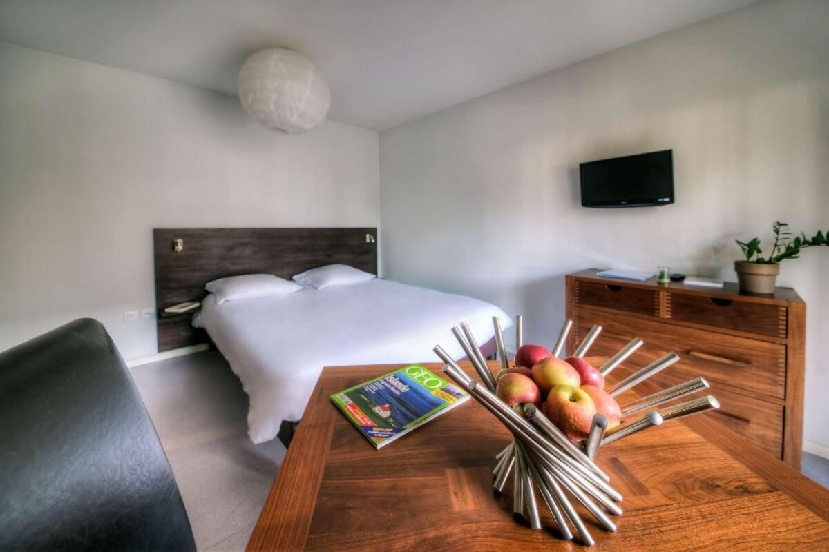 Ein Hotelzimmer mit einem Bett, einer Holzkombination, einem Tisch mit Äpfeln und einer Zeitschrift sowie einem Fernseher an der Wand.