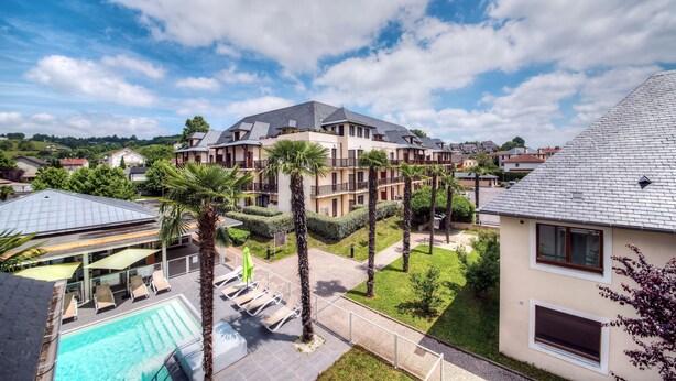 A multi-story hotel with a swimming pool, palm trees, and a clear blue sky.
