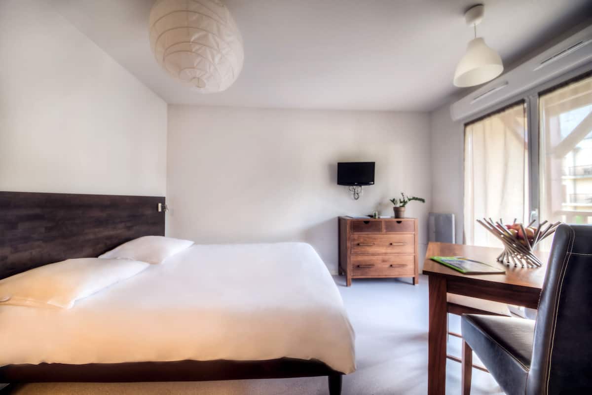Habitación de hotel con una cama grande, un aparador de madera, un escritorio con silla, un televisor de pantalla plana en la pared y una ventana con cortinas.