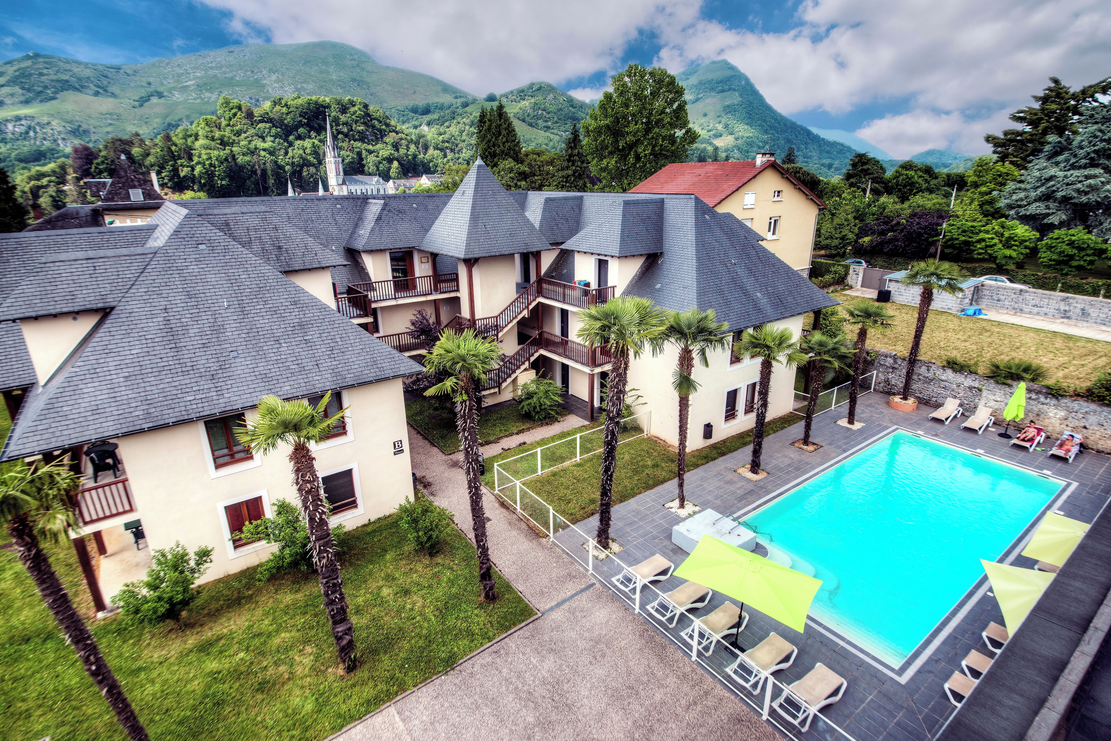 Un hotel con varias edificaciones, una piscina y montañas al fondo.