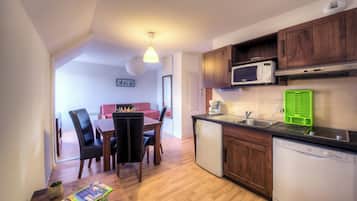 Cocina compacta con armarios de madera, microondas, cafetera y lavavajillas.