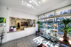 Uma área de recepção com balcão, quadro de informações fixado na parede e uma vitrine de vidro com objetos.