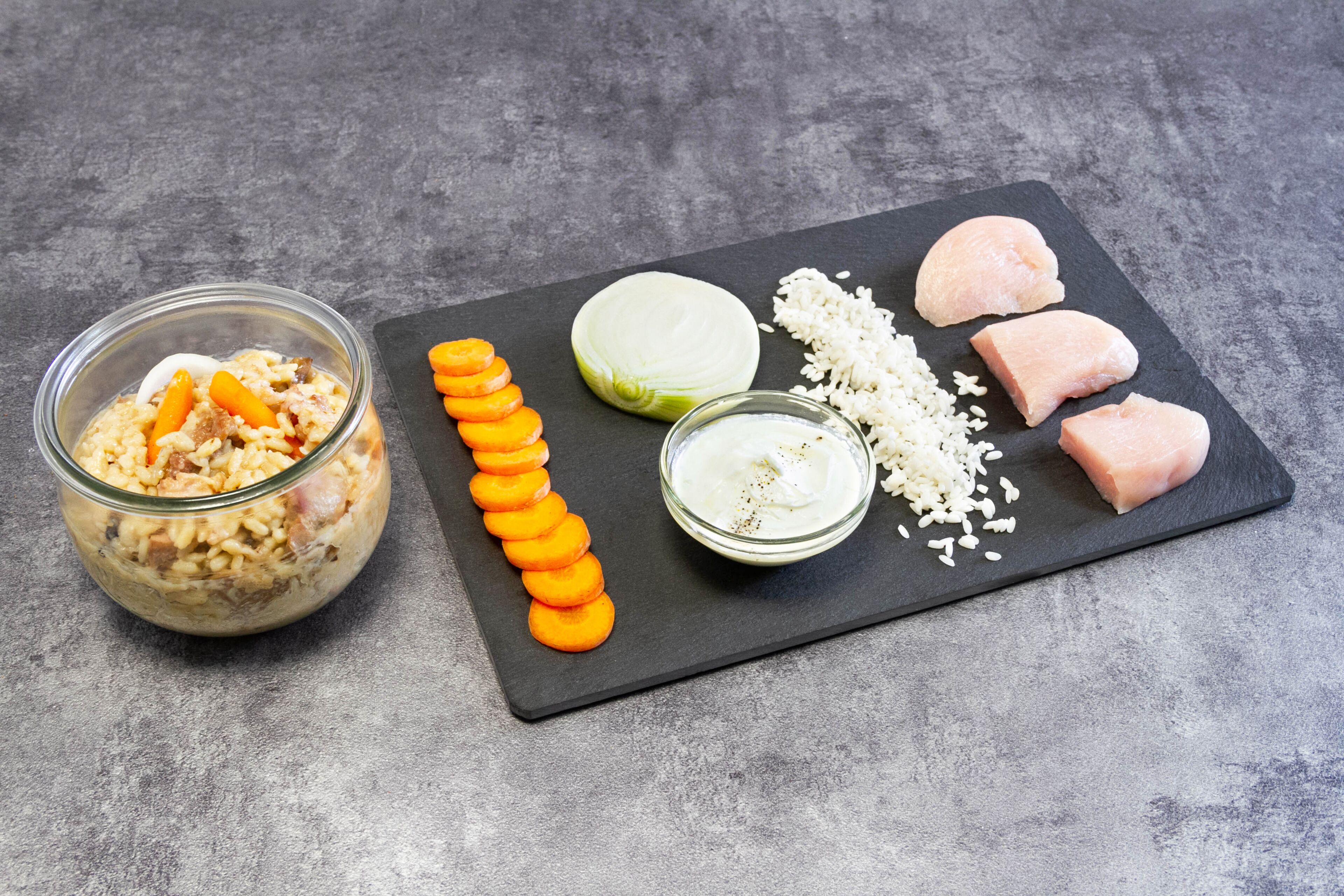 Eine Mahlzeit mit Reis, Hähnchen, Karotten und einer cremigen Soße auf einer Schieferplatte.