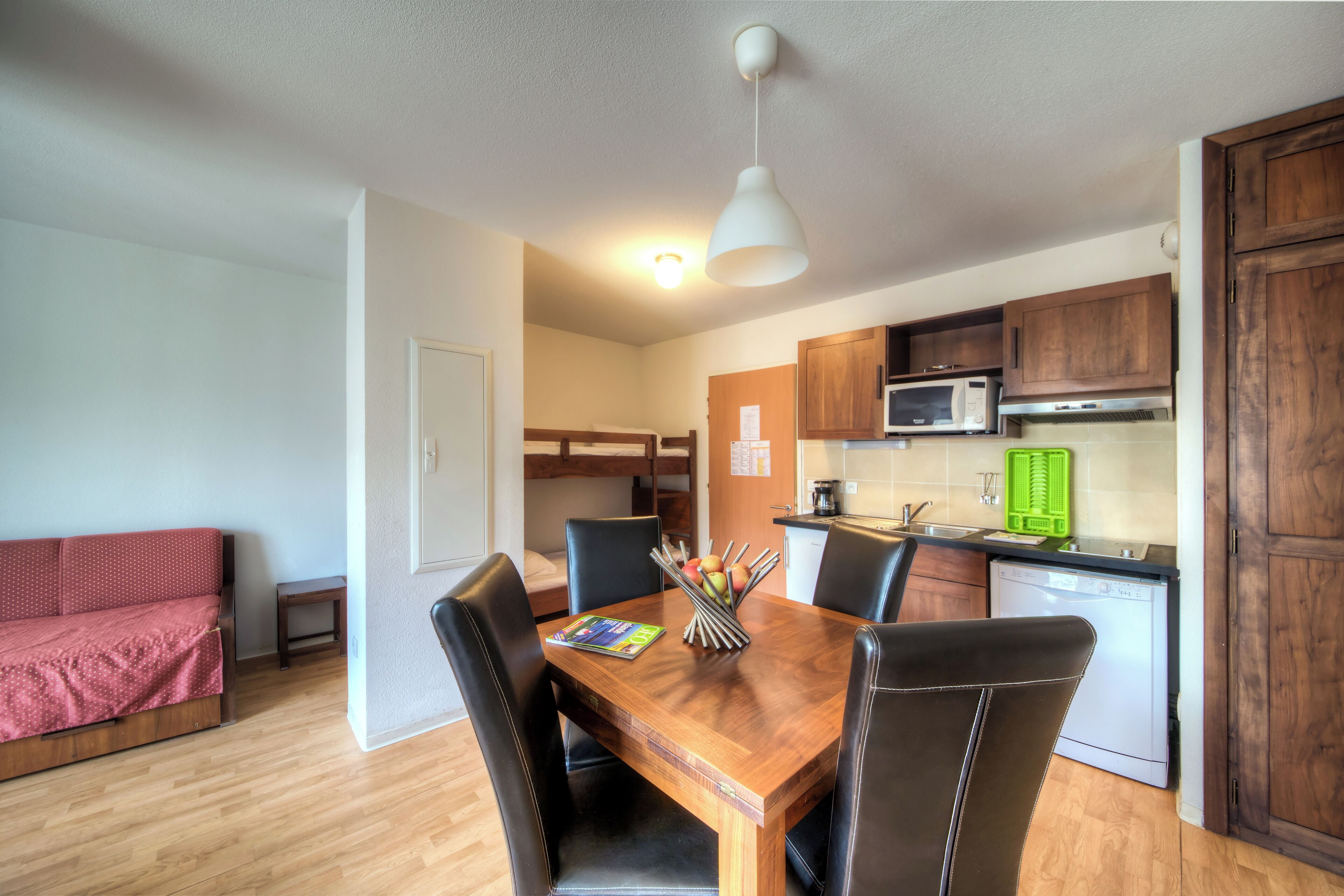 Un espace de vie compact comprenant un coin repas, une kitchenette et un canapé rouge.