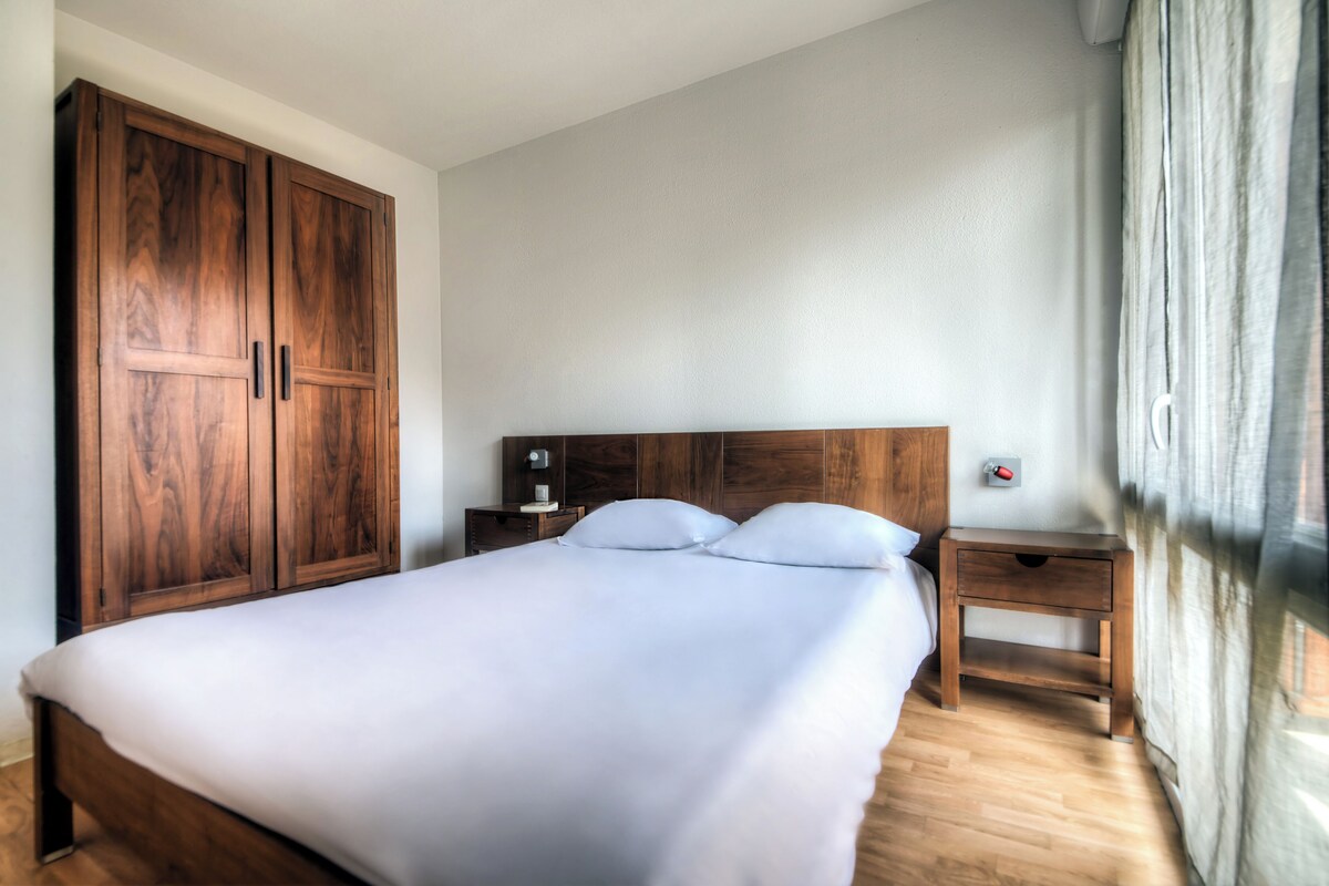 Ein Schlafzimmer mit einem großen Bett, einem Holzschrank, Nachttischen und einem Fenster mit Vorhängen.