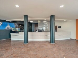 A hotel reception area with a counter, two pillars, and a mural of a building. - B&B Hotel Settimo Torinese (Settimo Torinese)
