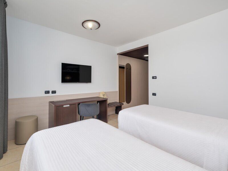 A hotel room with two beds, a desk, a TV, and a trash bin.