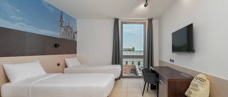 A hotel room with two beds, a desk, a chair, a TV, and a balcony with a view.