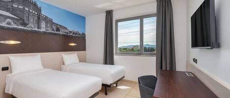 Habitación de hotel con dos camas, un escritorio, una silla, un televisor y una ventana con cortinas.