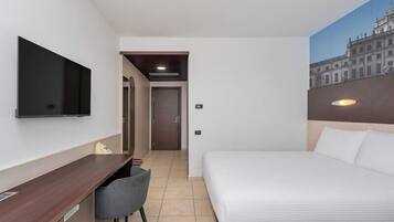 Ein Hotelzimmer mit einem Bett, einem Schreibtisch, einem Sessel, einem Fernseher und einem Bild an der Wand.