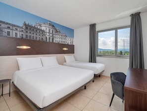 A hotel room with two beds, a desk, a chair, a large window with curtains, and a mural on the wall.